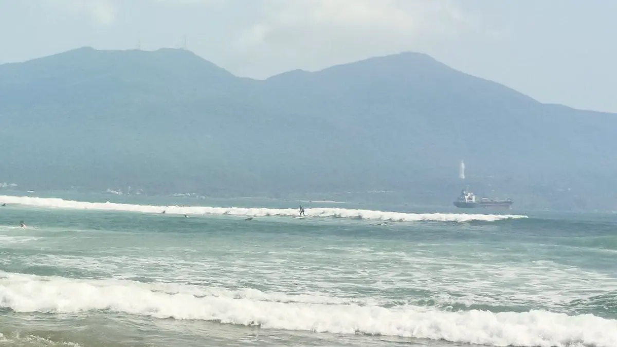 Surfer riding a small wave at My Khe Beach with Sơn Trà Peninsula in the background